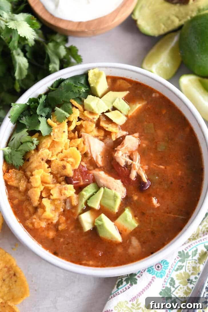 Easy Chicken Tortilla Soup Instant Pot Stovetop Slow Cooker 2 Top down view of a white bowl full of chicken tortilla soup topped with diced avocados, crushed chips, and chopped cilantro.