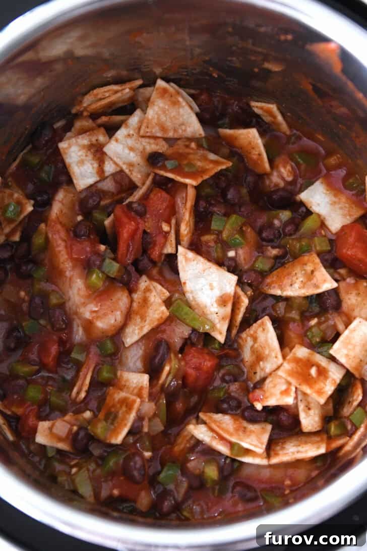 Easy Chicken Tortilla Soup Instant Pot Stovetop Slow Cooker 4 Top down view of an InstantPot filled with raw chicken, black beans, crushed tomatoes, green chiles, and cut up tortillas.