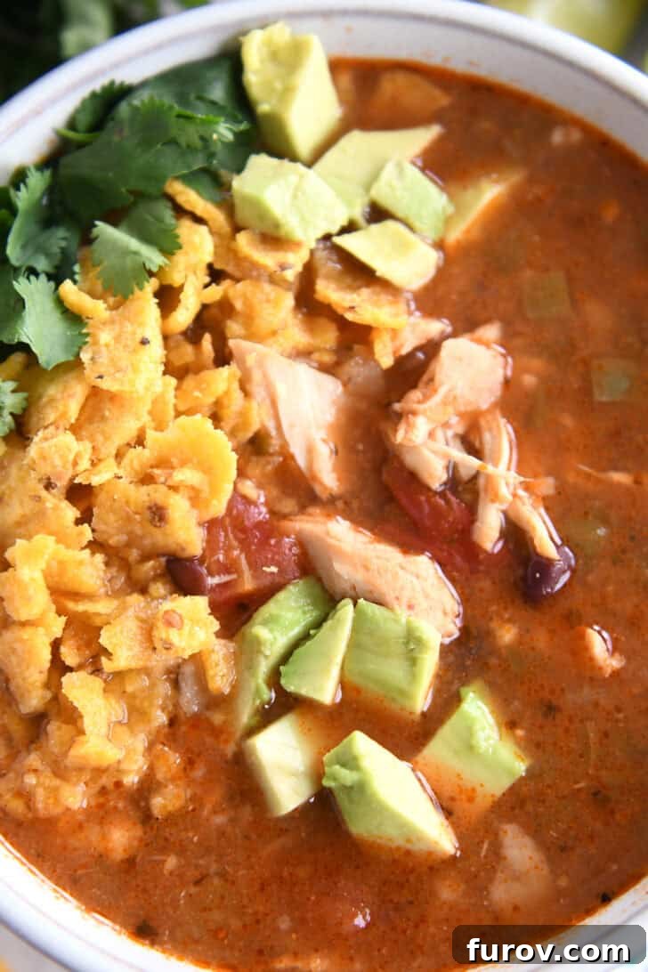 Easy Chicken Tortilla Soup Instant Pot Stovetop Slow Cooker 7 Top down view of a white bowl full of chicken tortilla soup topped with diced avocados, crushed chips, and chopped cilantro.