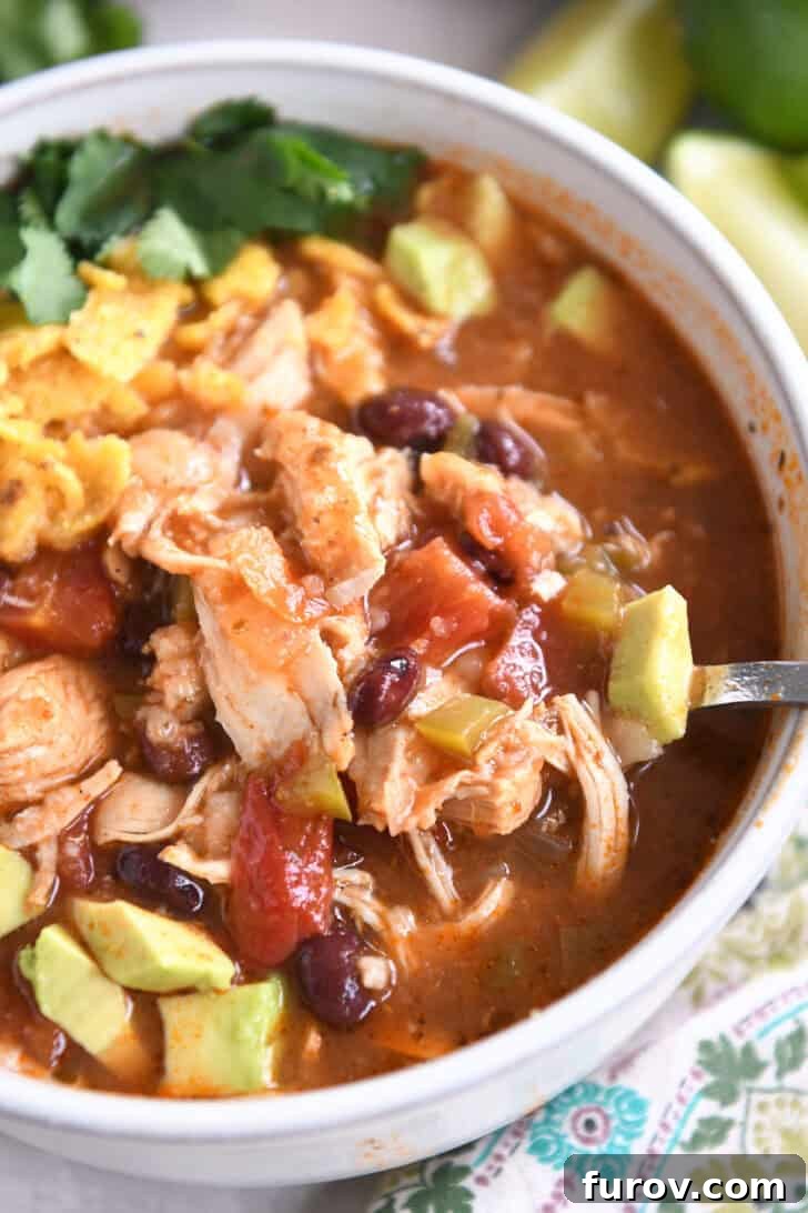 Easy Chicken Tortilla Soup Instant Pot Stovetop Slow Cooker 8 Top down view of a white bowl of chicken tortilla soup topped with diced avocados, crushed chips, and cilantro.