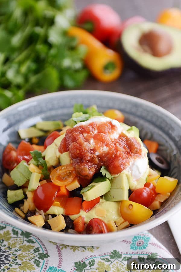 A vibrant bowl brimming with chopped vegetables, creamy avocado, ripe tomatoes, fresh cilantro, zesty salsa, and a dollop of sour cream, promising a delicious and healthy meal.