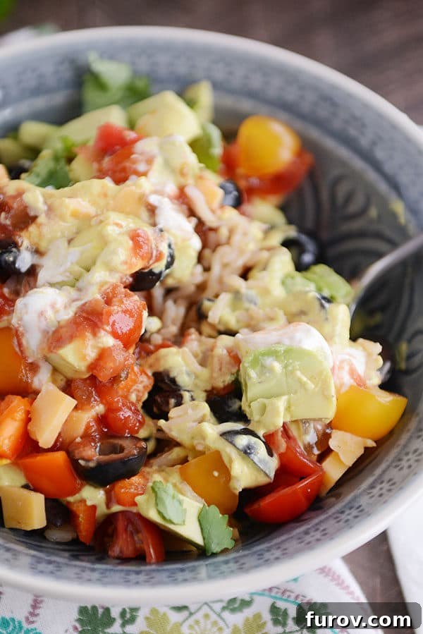 A beautifully composed bowl of rice, adorned with generous cubes of cheese, thinly sliced olives, creamy avocado, fresh tomatoes, and a vibrant salsa, ready to be enjoyed.