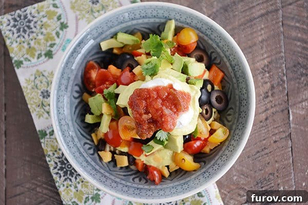 A close-up view of a wholesome Yum Yum Bowl, featuring a colorful array of chopped vegetables, sliced olives, creamy avocado, juicy tomatoes, fresh cilantro, salsa, and a dollop of sour cream.