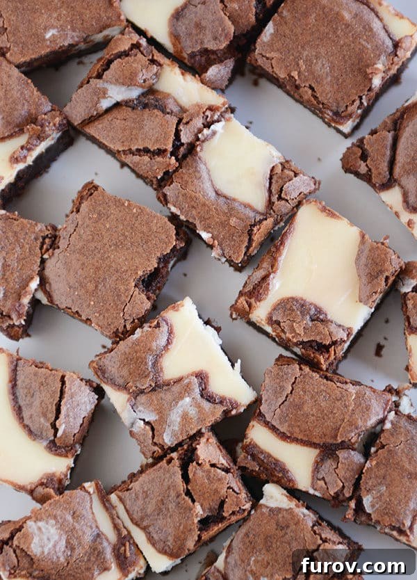 Top view of a bunch of square cream cheese chocolate brownies on a white platter.