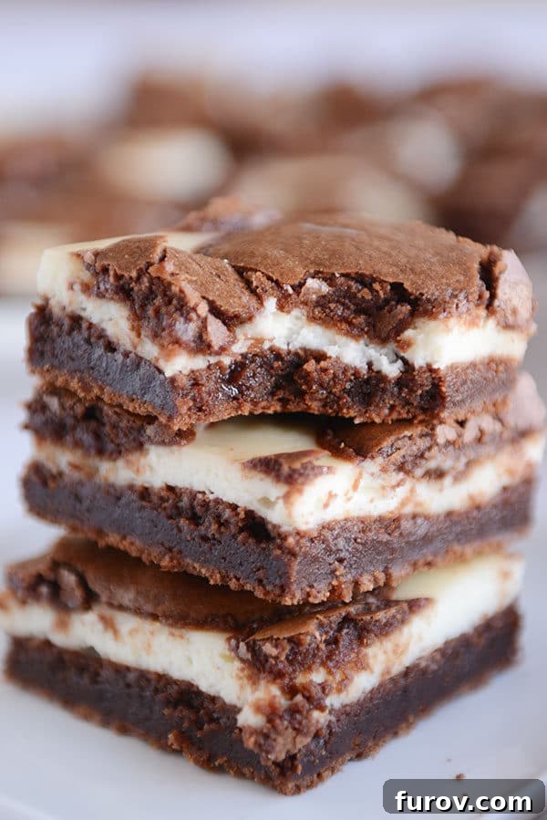 Three cream cheese chocolate brownies stacked on top of each with the top one with a bite taken out.