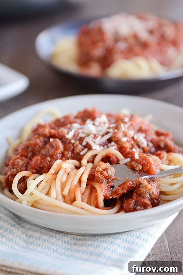 Speedy Homemade Weeknight Marinara 2 A fork twirling a bite of spaghetti noodles in a white bowl, topped with generous amounts of meaty spaghetti sauce and grated Parmesan cheese. The presentation emphasizes a quick, satisfying meal.