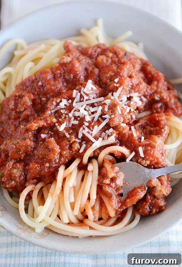 Speedy Homemade Weeknight Marinara 5 A fork gracefully twirling a perfect bite of spaghetti noodles in a white bowl, adorned with savory meaty spaghetti sauce and a generous sprinkle of Parmesan cheese.