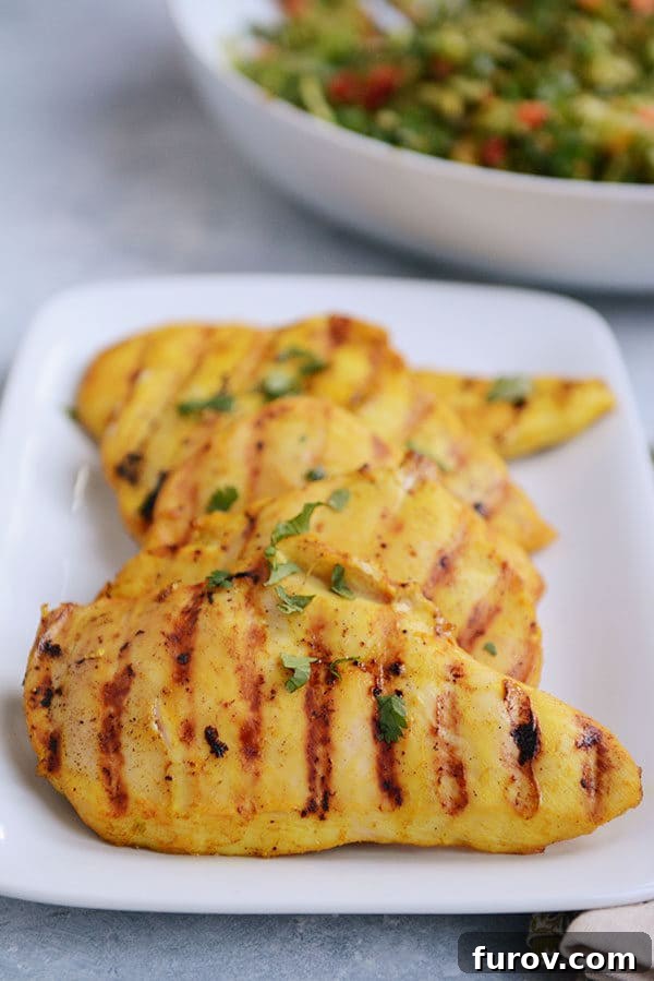 A white platter filled with golden grilled chicken pieces, generously sprinkled with fresh cilantro. 