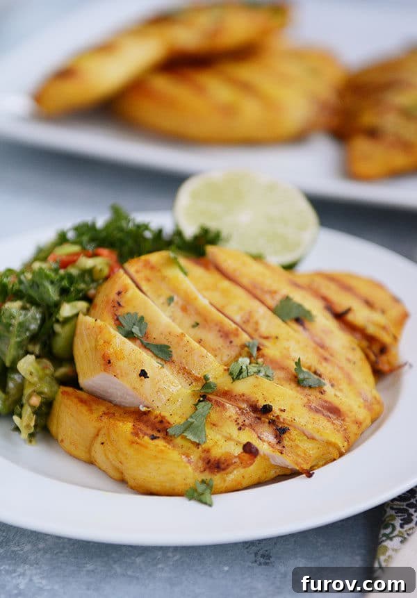 A white plate with perfectly sliced grilled chicken, a fresh green salad, and a bright slice of lime for garnish.