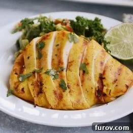A white plate with sliced grilled chicken and a green salad and slice of lime on the plate.