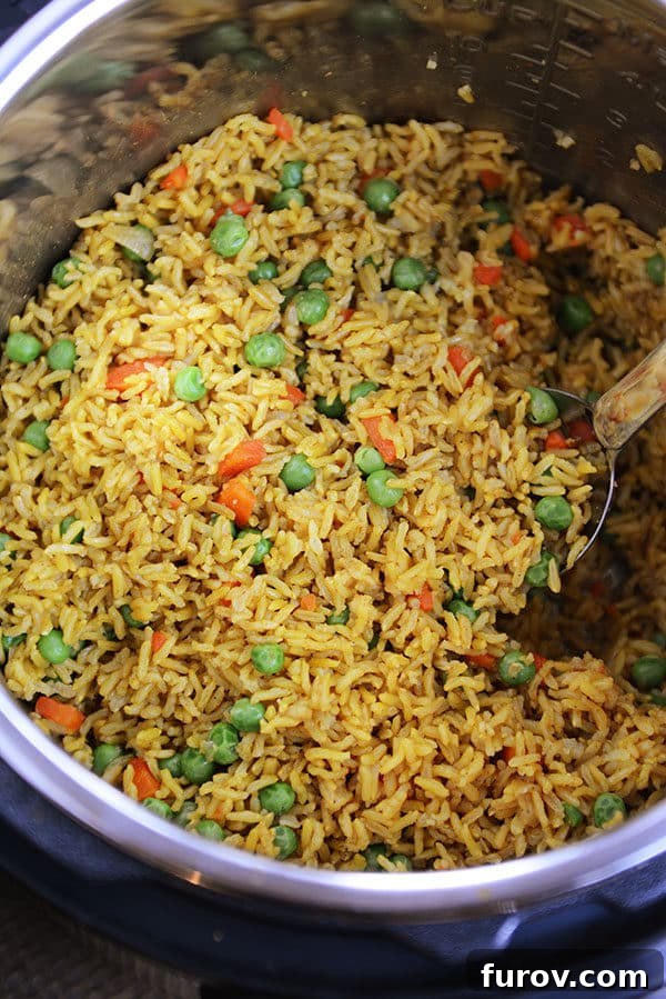 A close-up of an Instant Pot inner pot filled with steaming, golden Indian vegetable rice, studded with colorful peas and finely diced carrots, ready to be served.