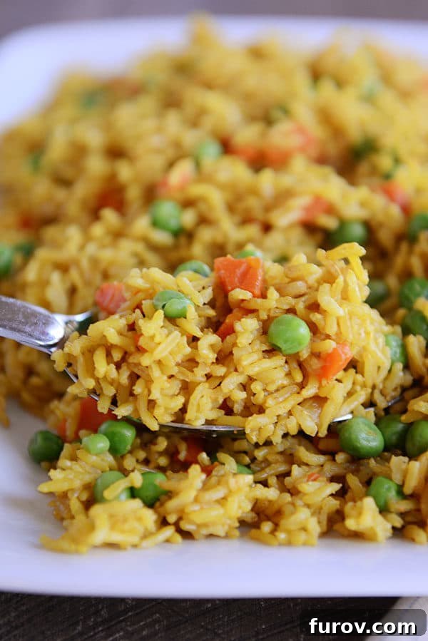 A serving spoon lifting a generous scoop of golden Indian vegetable rice, adorned with bright green peas and orange carrot pieces, showcasing its delightful texture and vibrant colors.