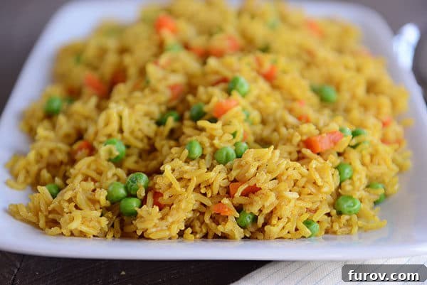A large white platter generously filled with golden-hued Instant Pot Indian vegetable rice, featuring a delightful mix of green peas and tender carrots, perfect for sharing.