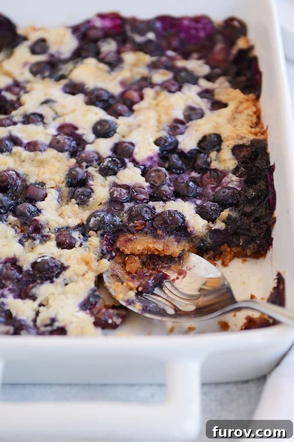 A large white baking dish with blueberry dump cake, a serving scooped out revealing the juicy blueberry layer.