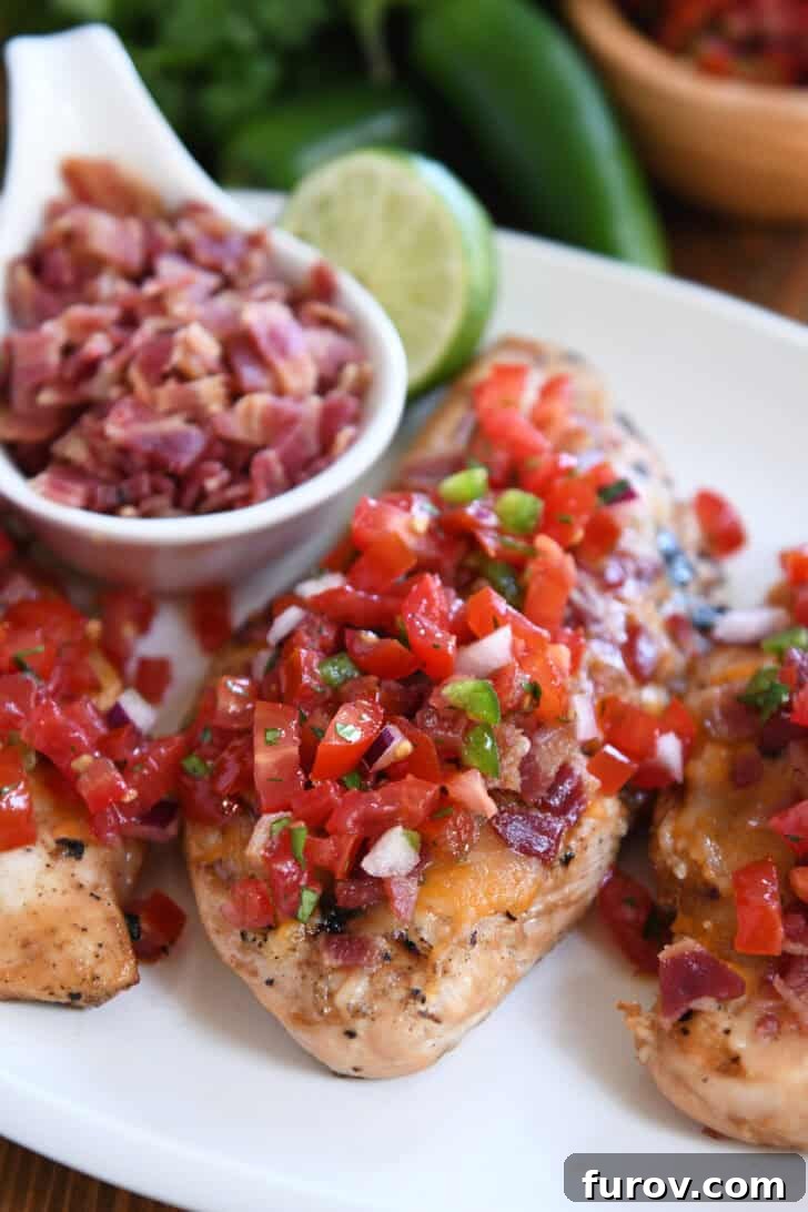 Grilled chicken breasts topped with fresh pico de gallo, melted cheese, and crispy bacon bits, served on a white plate with a side of lime wedges.