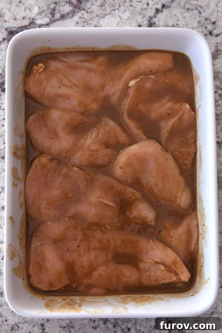Chicken breasts soaking in a savory marinade in a white baking dish, ready for grilling.