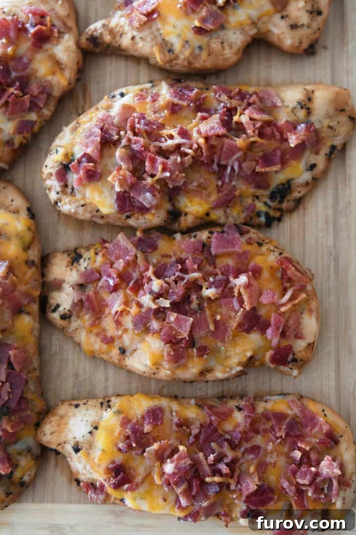 Freshly grilled chicken breasts adorned with melted Monterey Jack cheese and crispy bacon bits on a cutting board.