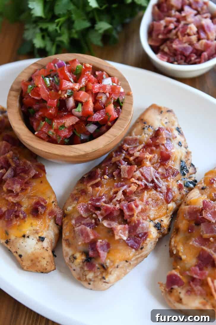 An overhead view of a complete Monterey Chicken dish with grilled chicken, melted cheese, bacon, and a generous side of pico de gallo.