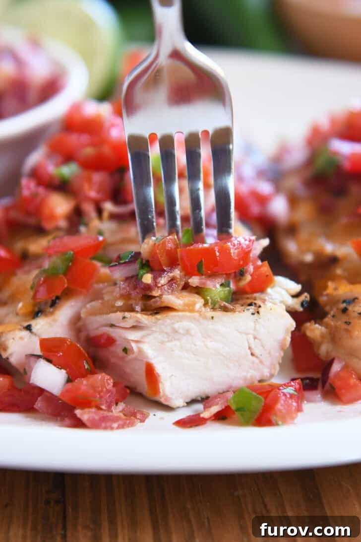 A close-up of a fork piercing a delicious bite of Monterey Chicken, showing layers of grilled chicken, melted cheese, crispy bacon, and fresh pico de gallo.
