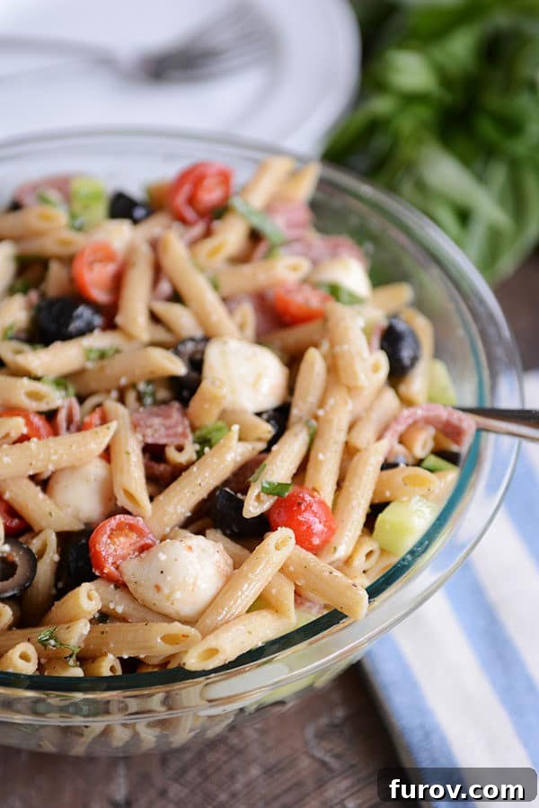 A glass bowl full of Italian pasta salad with olives, tomatoes, and mozzarella. A fresh, vibrant dish perfect for any meal.