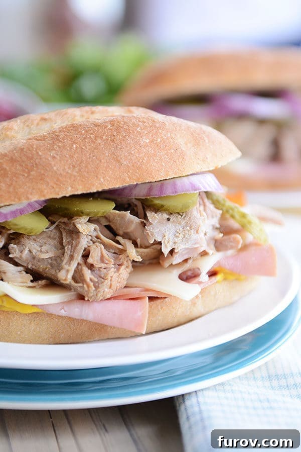 Perfect Slow Cooker and Instant Pot Cuban Sandwiches 2 A perfectly assembled Cuban sandwich filled with tender pork, melted Swiss cheese, crisp pickles, and thinly sliced onions on a white plate, ready to be enjoyed.