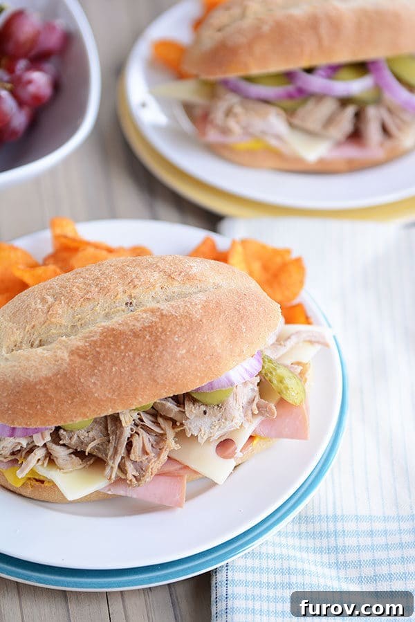 Perfect Slow Cooker and Instant Pot Cuban Sandwiches 3 Top-down view of a golden-brown Cuban sandwich nestled on a hoagie bun, accompanied by a small serving of potato chips on a clean white plate.
