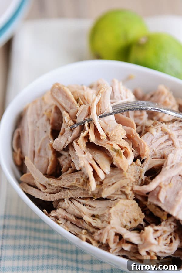 Perfect Slow Cooker and Instant Pot Cuban Sandwiches 4 A pristine white oval dish brimming with shredded, succulent mojo pork, showcasing its tender texture and rich color.