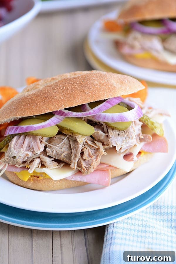 Perfect Slow Cooker and Instant Pot Cuban Sandwiches 5 A generously filled Cuban sandwich on a crisp hoagie bun, artfully arranged on a white plate, inviting you to take a bite.