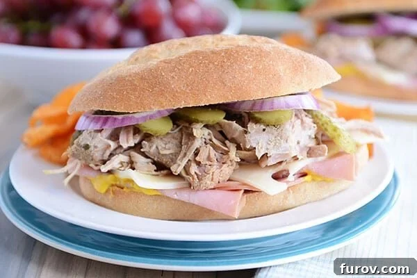 Perfect Slow Cooker and Instant Pot Cuban Sandwiches 7 A close-up of a perfectly stuffed Cuban sandwich, showcasing the layers of rich pork, ham, cheese, and pickles within a golden hoagie bun, resting on a white plate.