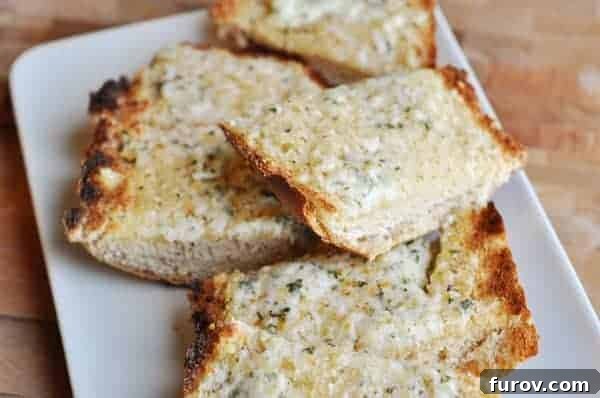 Slices of golden-brown baked cheesy garlic bread on a white plate, showcasing the perfectly melted cheese and crusty exterior, ready to be served.