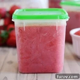 A clear plastic container filled with vibrant red strawberry freezer jam.