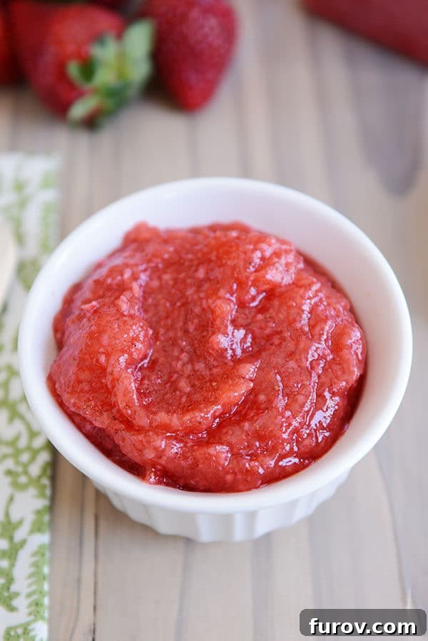 A glistening white ramekin filled with homemade strawberry freezer jam, showcasing its vibrant red color and smooth texture. Ready to be enjoyed.