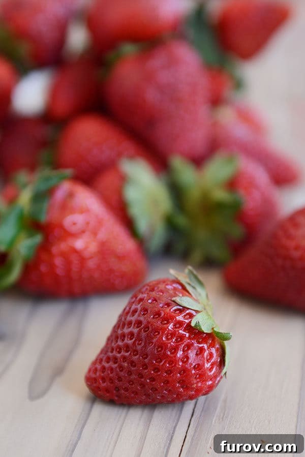 A bounty of fresh, ripe red strawberries scattered on a rustic wooden countertop, ready for making delicious jam.
