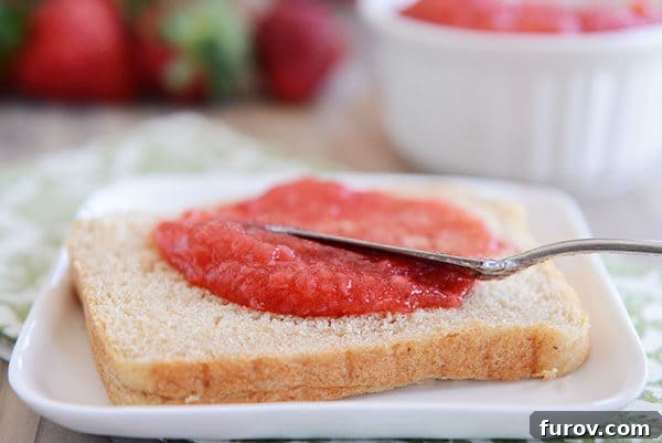A knife gently spreading vibrant red strawberry jam over a slice of whole wheat bread, highlighting its smooth texture and delicious appearance.