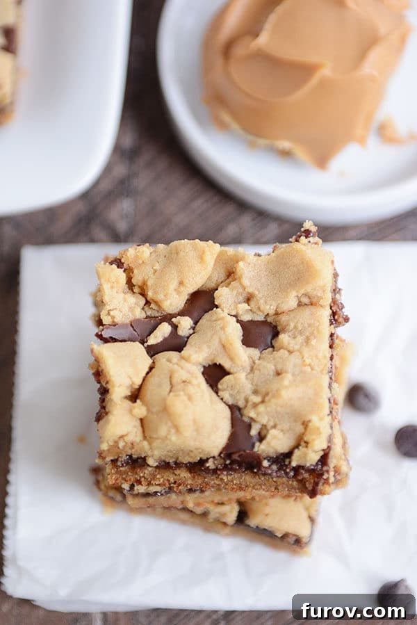 A stack of golden brown peanut butter fudge bars with rich chocolate layers, on parchment paper.