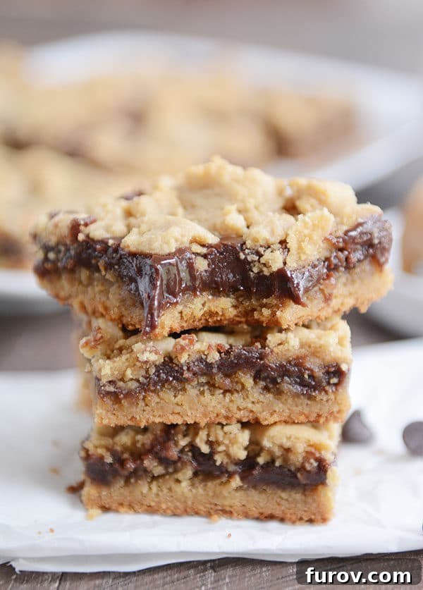 Three layered peanut butter fudge bars stacked, with a bite taken from the top bar, revealing the soft cookie and rich fudge.