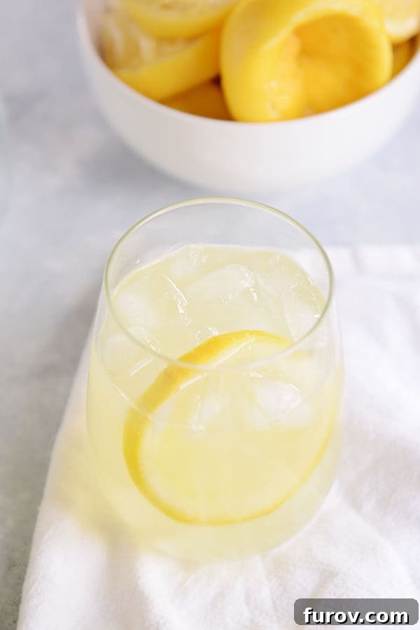 A small glass of lemonade and a bowl of juiced lemons behind it.