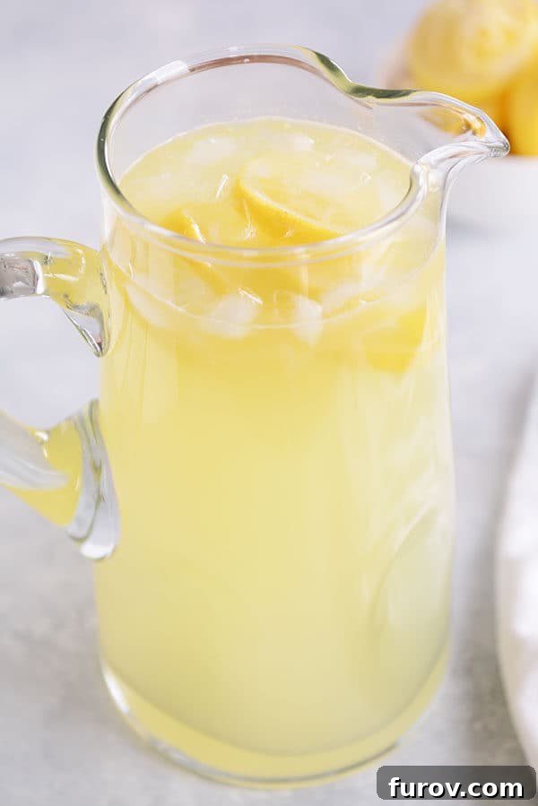 A glass pitcher of fresh lemonade with ice and lemon slices. 