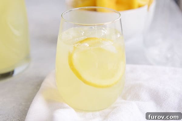 A glass of lemonade with ice and a slice of lemon in it.