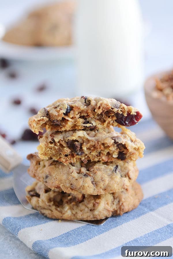 A stack of chewy granola cookies on a blue and white napkin with the top cookie split in half, revealing their delicious texture.