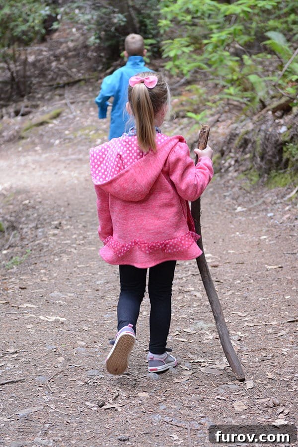 Effortless Wonders: Your Relaxed Guide to the Redwood Giants 16 A determined little girl hikes uphill with a walking stick, her face focused as she navigates the forest path.