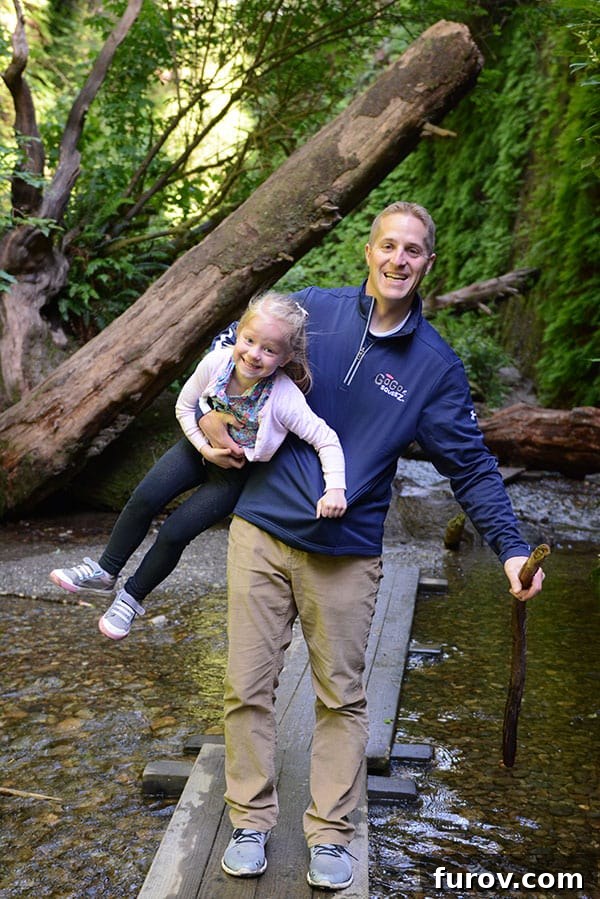 Effortless Wonders: Your Relaxed Guide to the Redwood Giants 19 A father carries his young daughter across a narrow wooden plank bridge over a shallow stream in Fern Canyon.