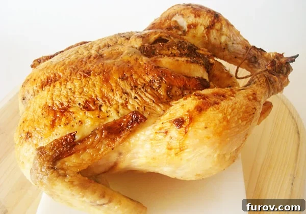 A beautifully golden-brown whole roasted chicken, glazed with honey, resting on a white cutting board, garnished with fresh herbs.