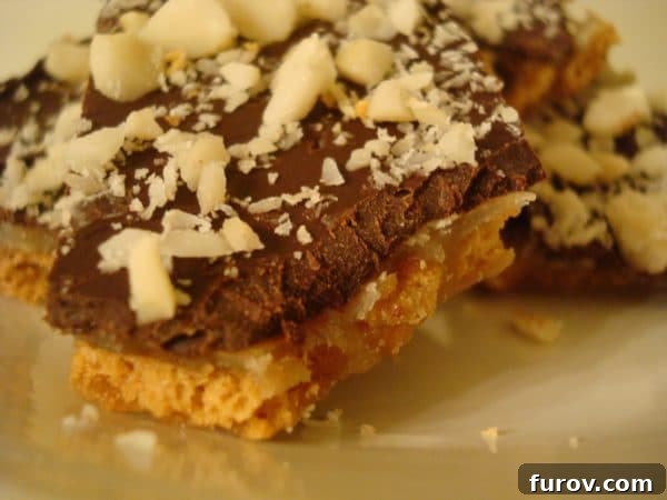 Chocolate toffee with almonds on top on a white plate, ready to be broken into pieces.