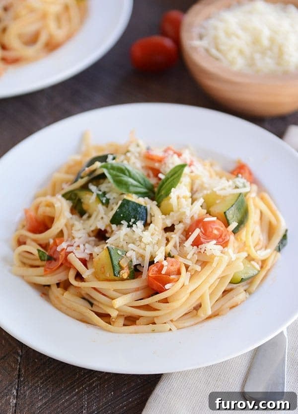 30-Minute Fresh Zucchini Tomato Linguine 2 A white plate of zucchini tomato pasta topped with parmesan cheese and basil leaves on a white plate.