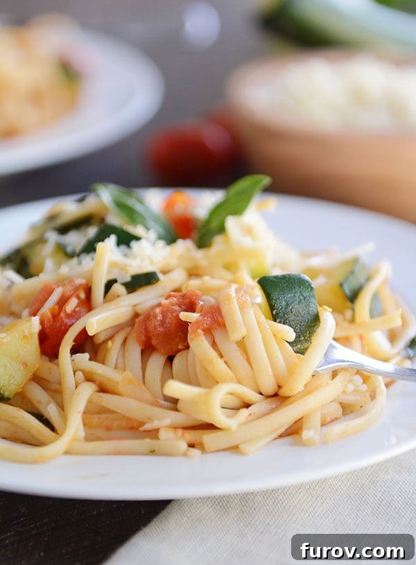 30-Minute Fresh Zucchini Tomato Linguine 3 A fork taking a bite of zucchini and tomato pasta off of a white plate.