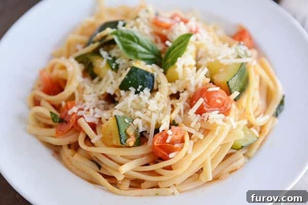 30-Minute Fresh Zucchini Tomato Linguine 6 A white plate of zucchini and tomato pasta topped with two basil leaves.