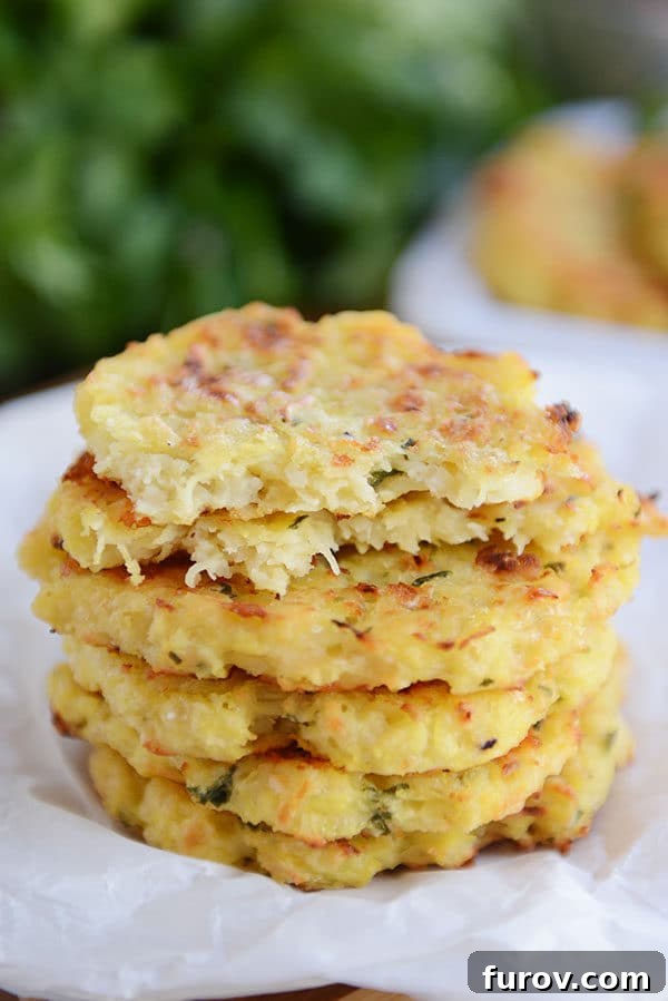 Crispy Baked Parmesan Spaghetti Squash Fritters 4 A stack of golden-brown spaghetti squash Parmesan fritters, with one fritter expertly split in half to reveal its tender, flavorful interior on a piece of parchment.