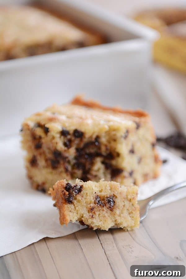 A fork taking a bite out of a piece of banana chocolate chip cake.