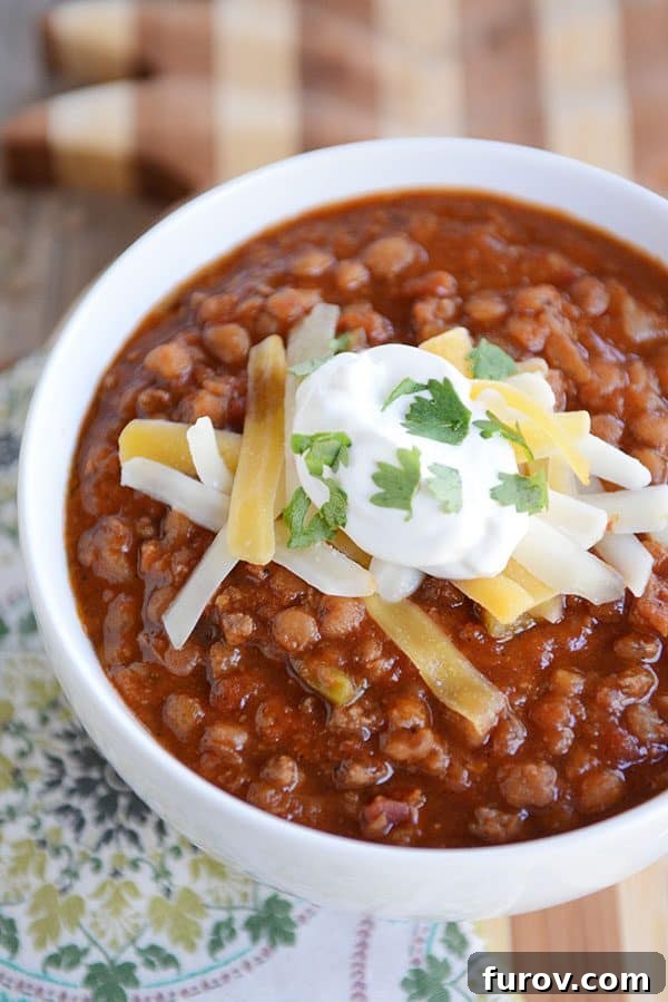 Instant Pot Lentil Chili Stovetop and Slow Cooker Variations 2 A white bowl full of sour cream and cheddar cheese-topped lentil beef chili.